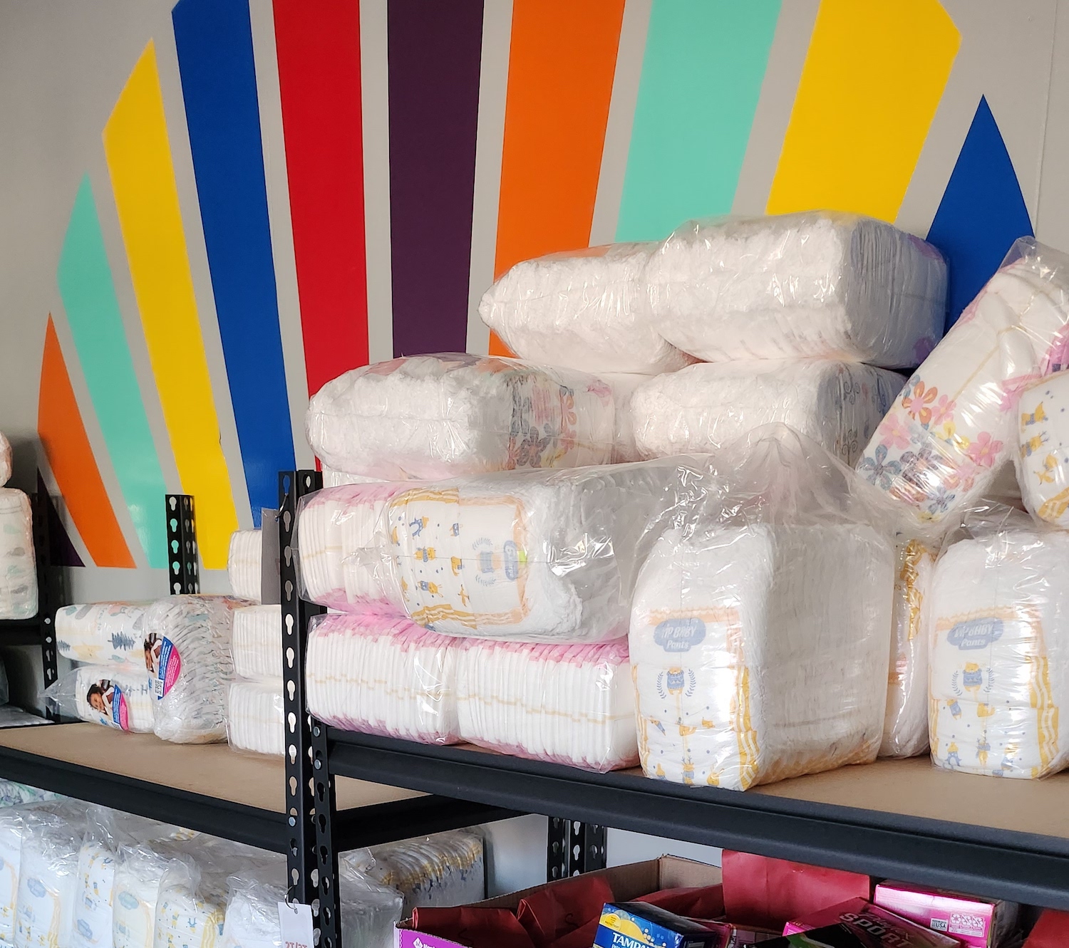 Image of diaper packs on shelf in front of All-Options logo painted on the wall